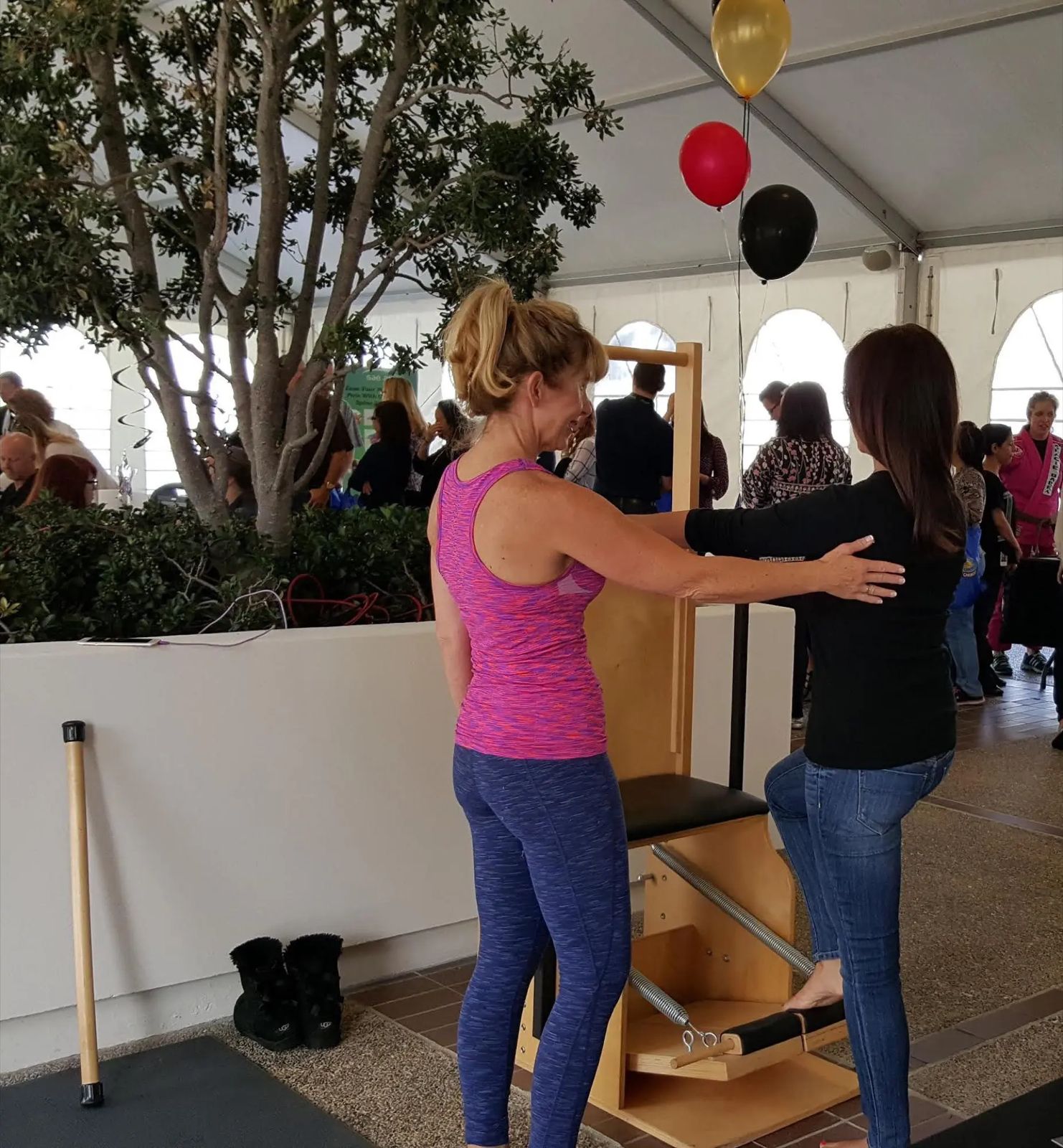 Pilates instructor coaching an employee under a tent with balloons