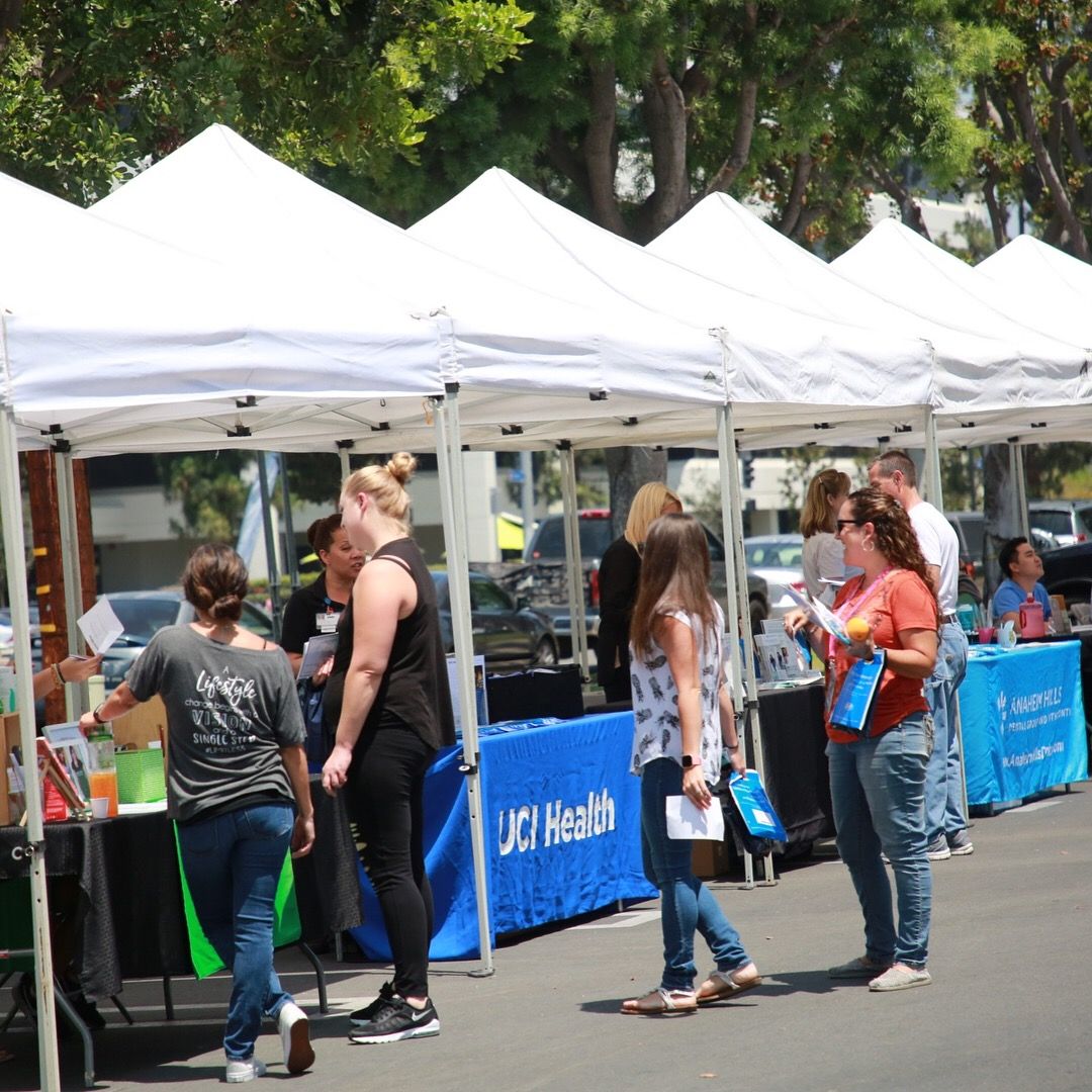 Row of white vendor tents with employees browsing wellness tables